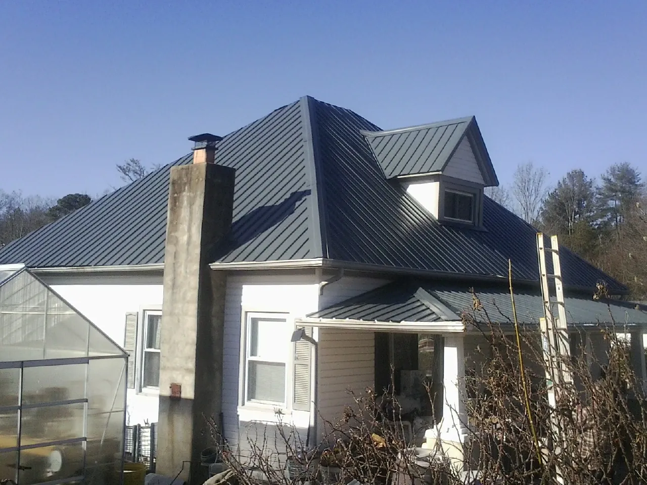 Dark blue standing seam metal roof on a white farmhouse with dormer — Slate & Tile Roof Repair by Roofing Brothers in Pleasant Shade