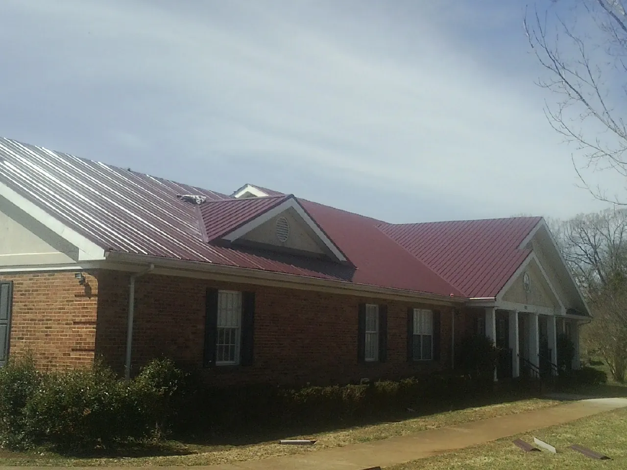 Red metal roof with gabled entries on a long brick building, from a Hail Damage Roof Repair job in Pleasant Shade