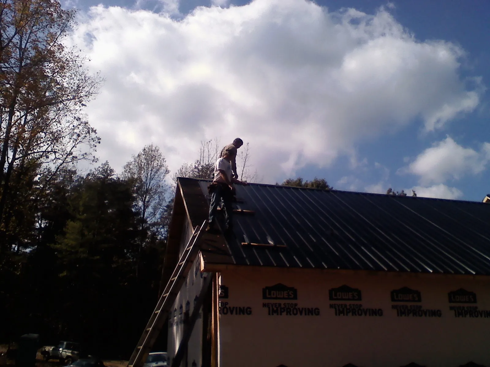 Roofer fastening dark metal panels high against a cloudy sky, from a Roof Inspection job in Pleasant Shade