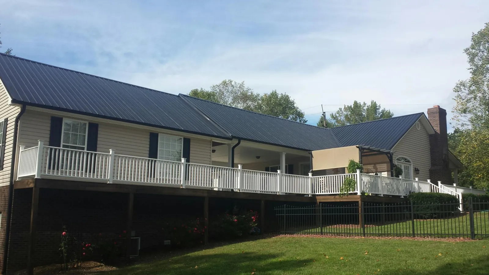 Black metal roof above a long white railed deck on a hillside home in Pleasant Shade