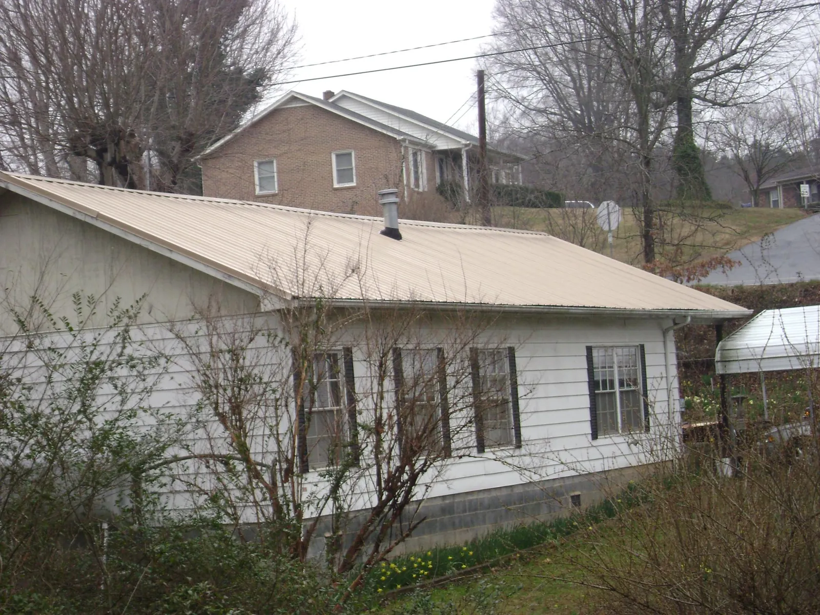 Tan metal roof on a white sided house set into a hillside — Commercial Roofing by Roofing Brothers in Pleasant Shade