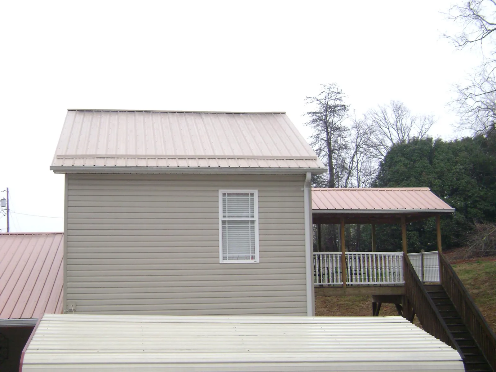 Tan metal roofs on a two story addition and attached porch, from a Roof Replacement job in Pleasant Shade